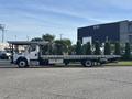 A 2022 Freightliner M2 106 flatbed truck with a white cab and a long flatbed trailer is parked on a paved surface