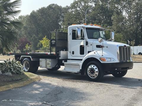 A 2020 Peterbilt 330 truck with a flatbed design featuring a black tool box and orange lights on the roof