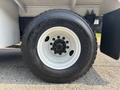 A close-up of a 2010 Freightliner M2 106 tire showing a black rim with multiple lug nuts and a treaded surface labeled with the tire brand and model