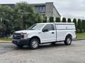 A white 2020 Ford F-150 with a fitted cap on the truck bed parked on the pavement