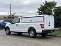A 2020 Ford F-150 in white with an enclosed bed cap parked on a street, showcasing its extended cab and steel wheels