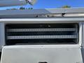 A white 2013 International 7500 with an open compartment featuring three horizontal shelves inside