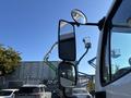 A 2006 Freightliner M2 106 truck with a large side mirror reflecting equipment in the background